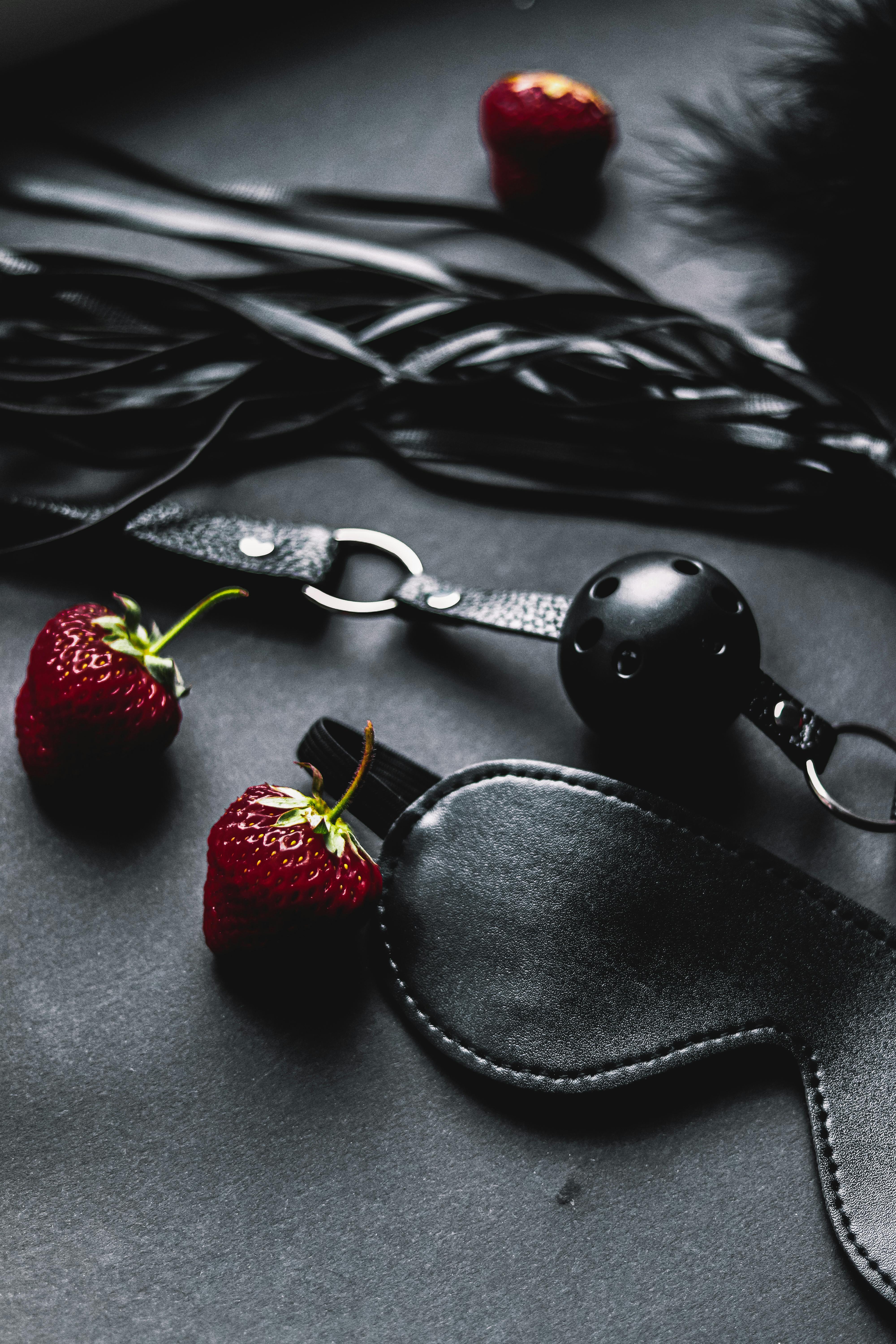 close up of leather sex accessories and strawberries on black background