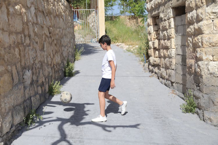 Boy In White T-shirt And Blue Shorts Playing Soccer Ball