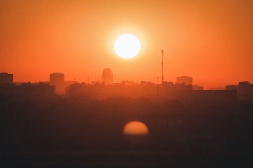 Free A stunning cityscape at sunset with an orange sky and visible sun casting a warm glow over silhouetted buildings. Stock Photo