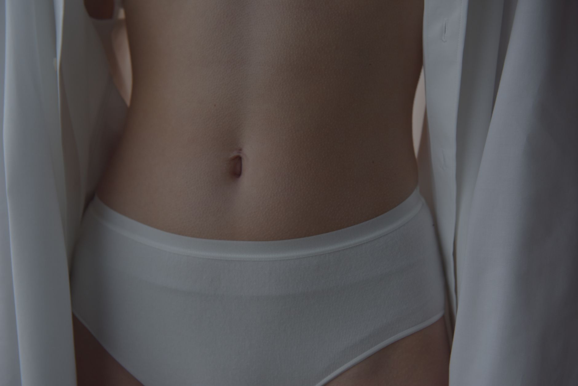 Intimate close-up image showcasing a woman's waist and belly button in white lingerie for fashion aesthetics.