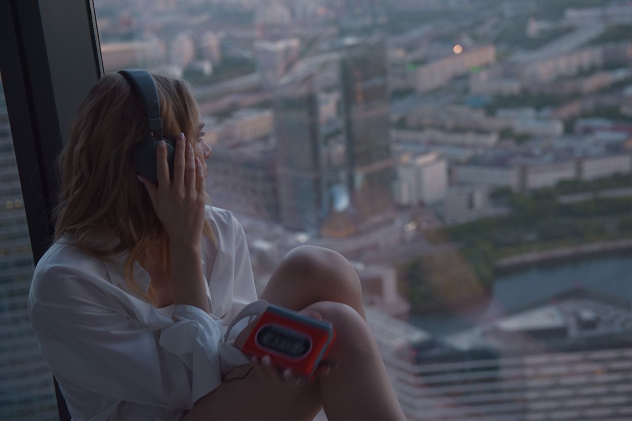 caucasian woman listening to music on a cassette player by a high rise