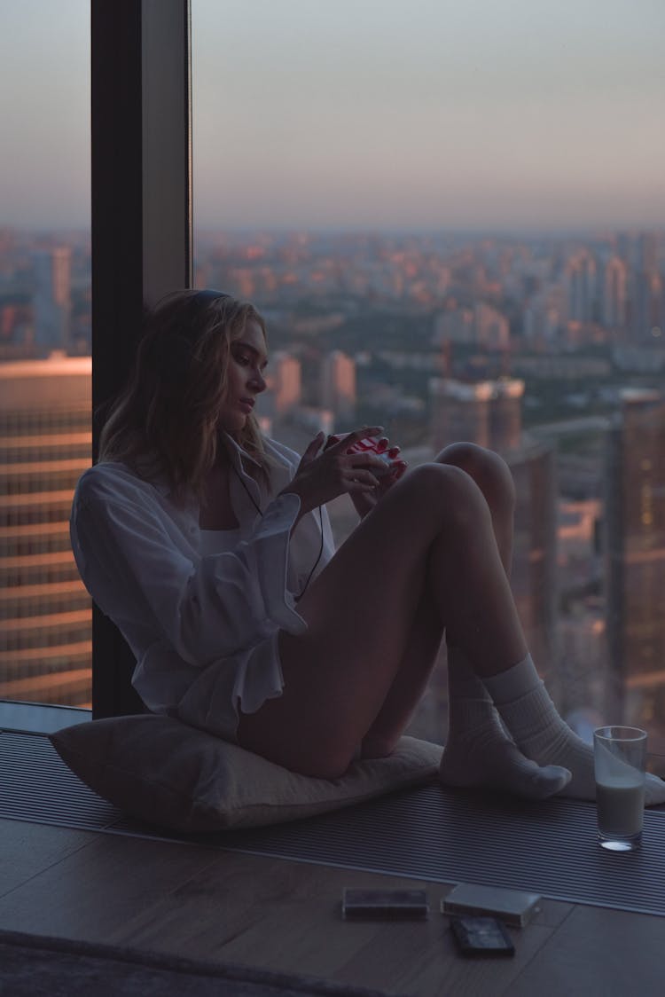 Woman Sitting On Pillow By The Window