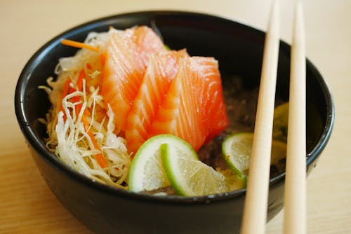 Free Slices of Salmon Sashimi with Slices of Lime on Black Bowl Stock Photo