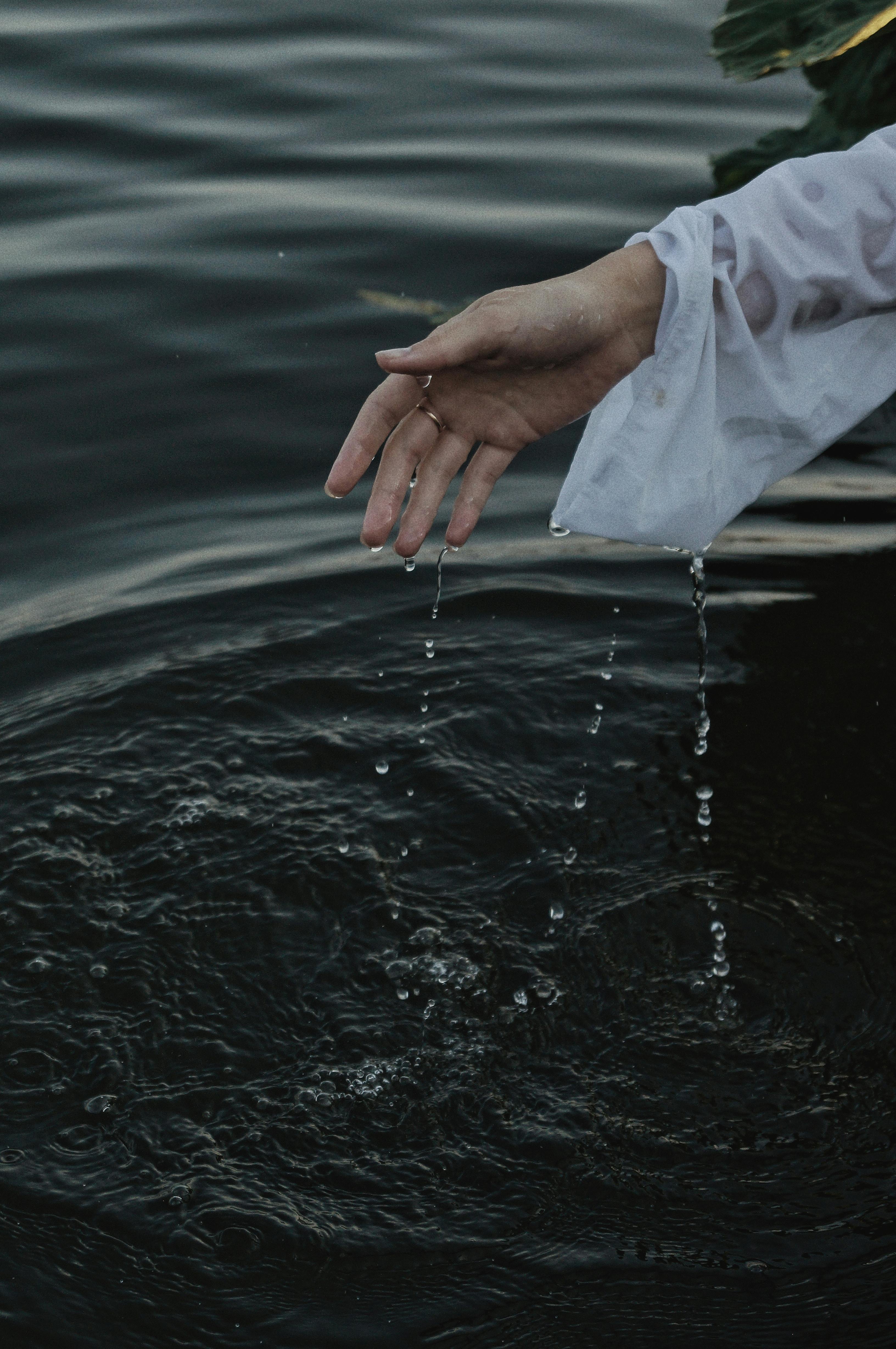 A graceful hand in a white sleeve elegantly drips water into tranquil ripples, creating a serene atmosphere.