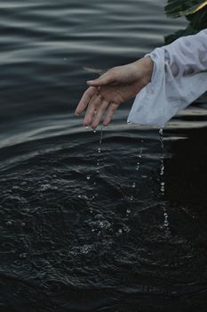 A graceful hand in a white sleeve elegantly drips water into tranquil ripples, creating a serene atmosphere.