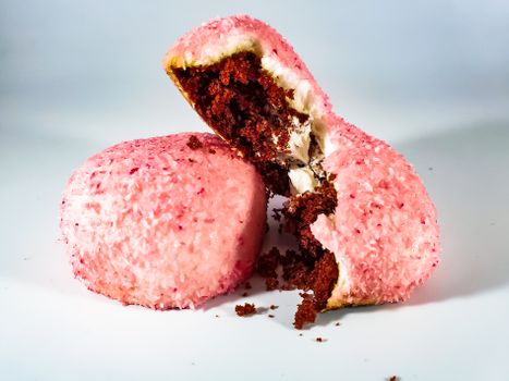Two pink coconut-covered chocolate pastries with cream filling on a white surface.