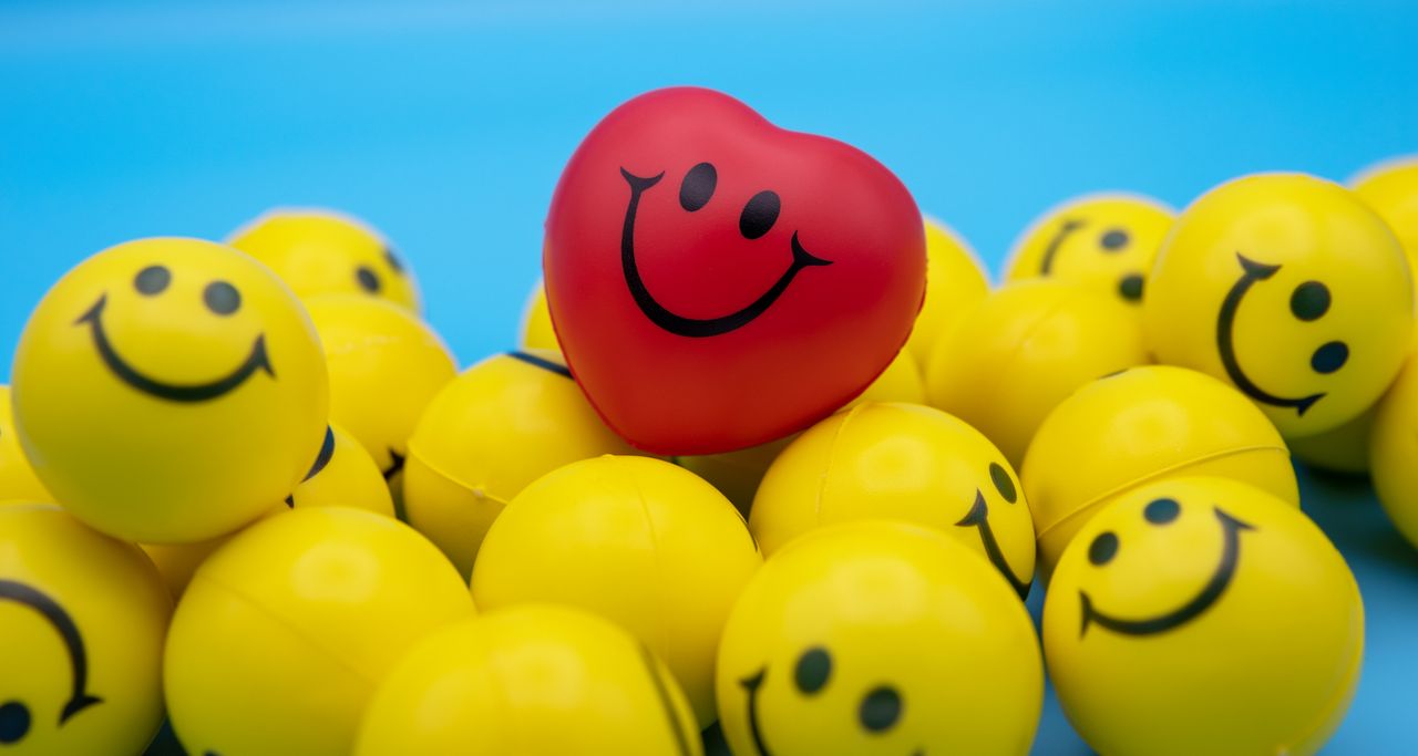a red heart shaped smiling ball stands out among yellow smiley faces s