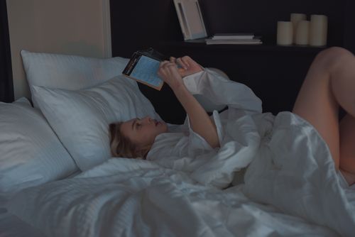 Free A woman comfortably reading a book in a cozy bedroom setting. Stock Photo