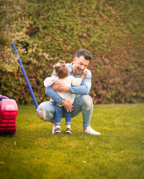 Free A father joyfully hugging his young daughter on a sunny day in a lush garden. Stock Photo