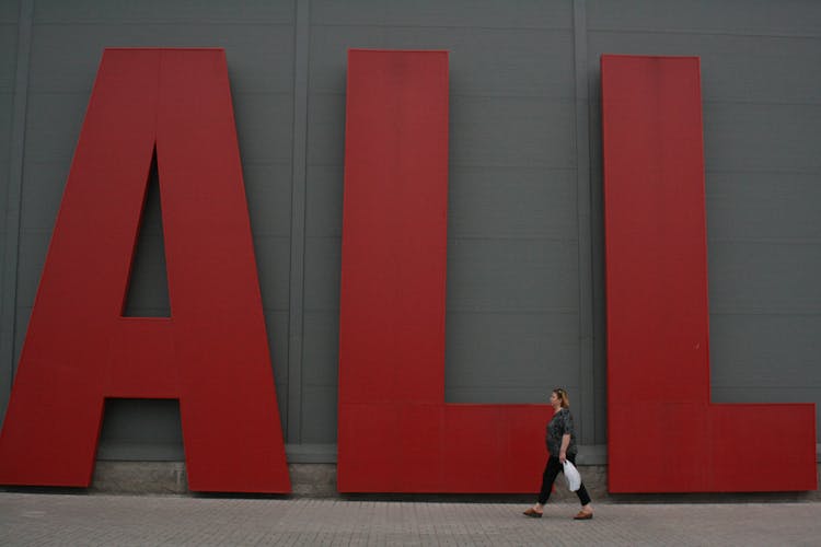 Woman Walking On Street Under Big Red Advertisement Letters