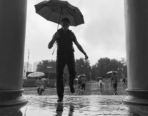 Free A Man Holding an Umbrella Walking on the Road with Water Stock Photo