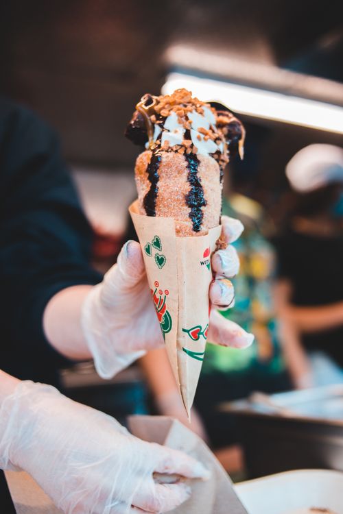 Free Close-up of a gloved hand holding a chocolate and nut coated ice cream cone at a street food market. Stock Photo
