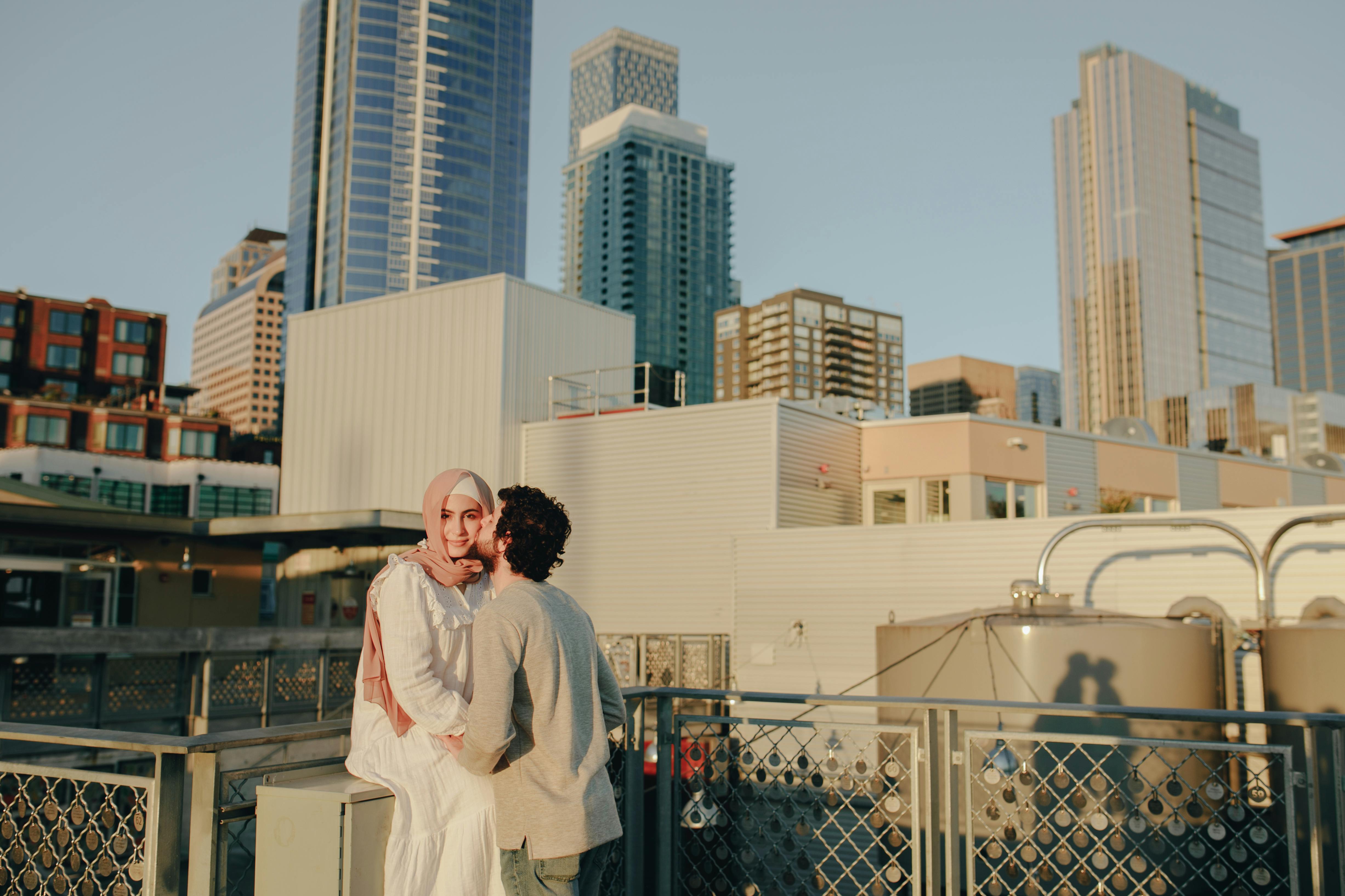 A romantic moment captured as a couple embraces on a rooftop with a city skyline backdrop.