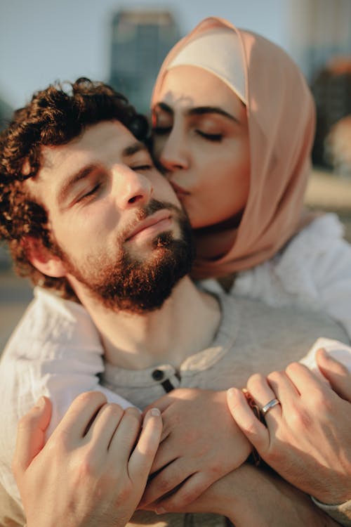 A Woman Wearing Hijab Kissing a Man from Behind