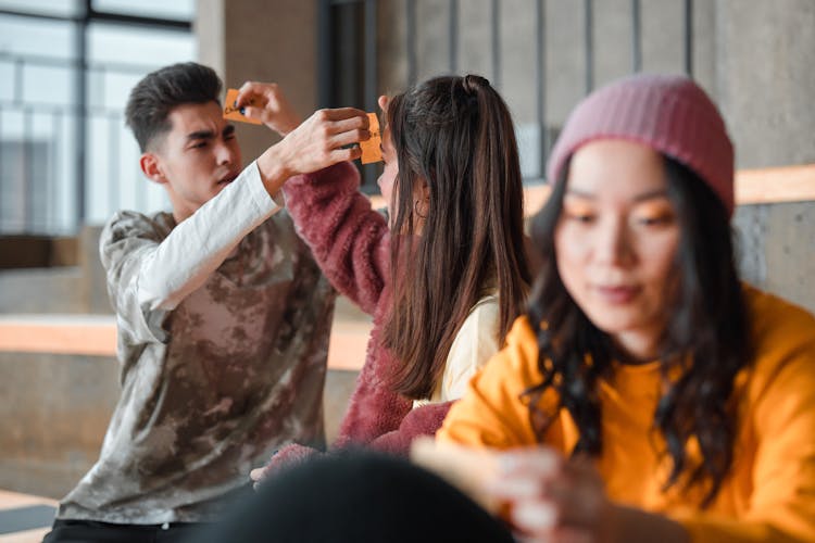 Women And Man Sitting And Putting Cards On Heads