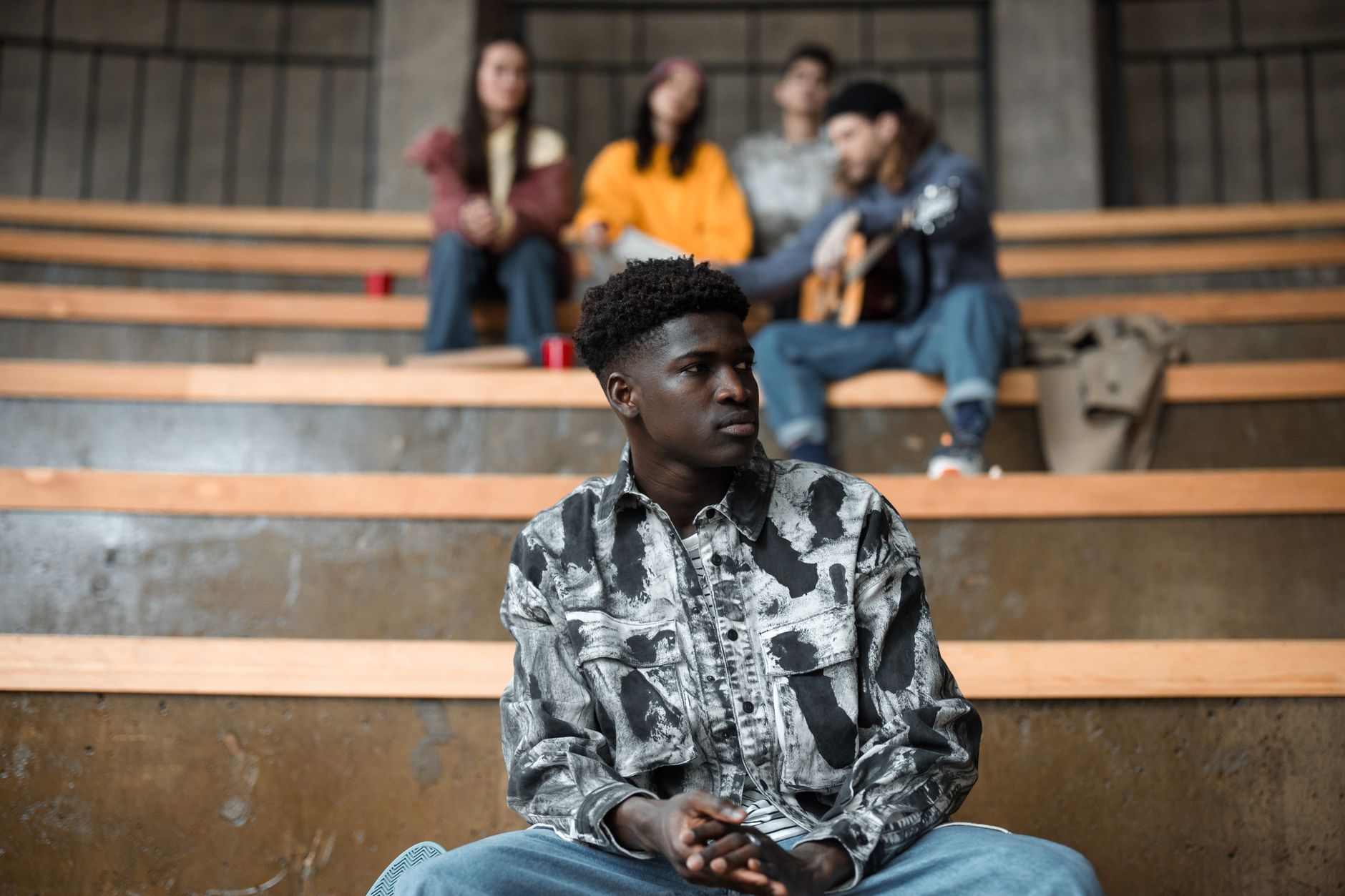 A young man sitting confidently on steps, with friends blurred in the background.