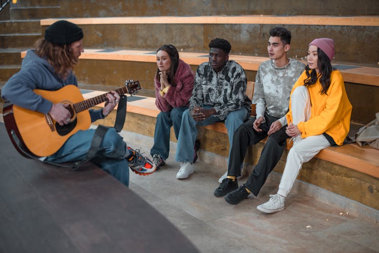 A Group Of Friends Watching A Man Playing The Guitar