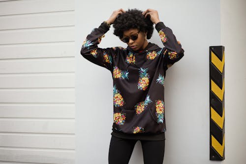 Free Photo of a Woman in Pineapple Print Pullover Leaning on White Wall Stock Photo