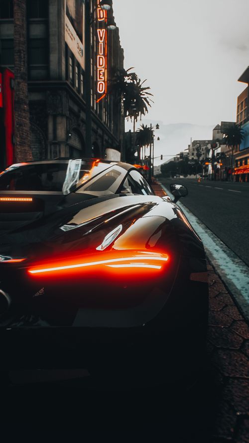 Free Luxury sports car with glowing tail lights parked on an urban street at dusk. Stock Photo