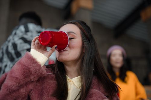 Free A stylish young woman drinks from a red cup during a lively indoor gathering. Stock Photo