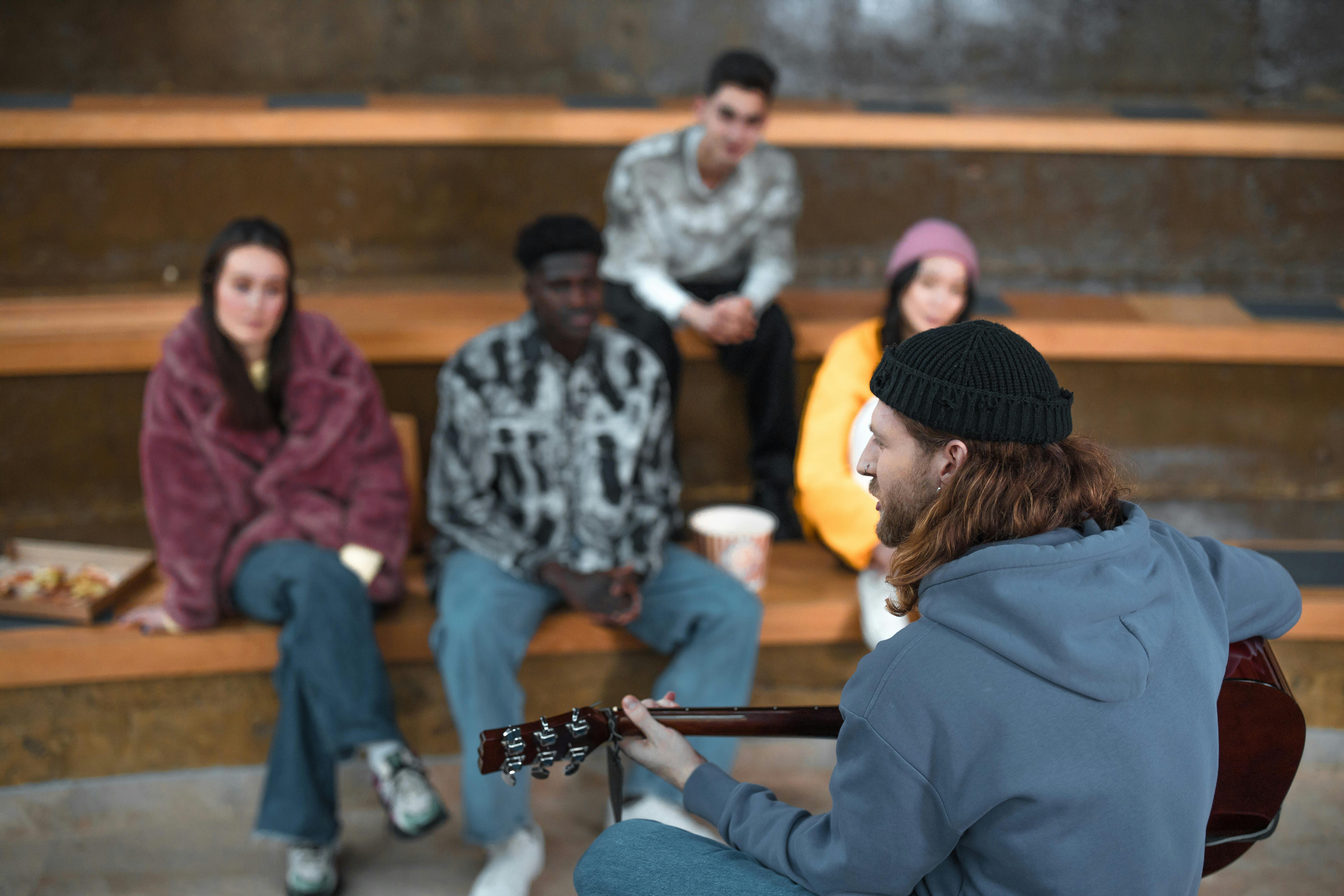 Free Group of diverse friends sitting outside, enjoying live guitar music in an urban amphitheater. Stock Photo