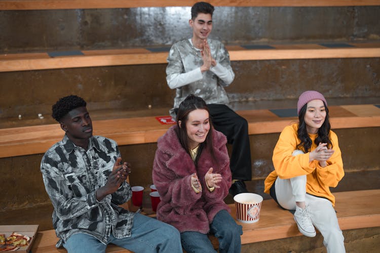 A Group Of Friends Sitting On Bleachers Clapping