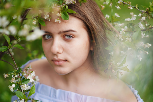 Free A young woman gazes through blooming branches, evoking a sense of natural beauty and tranquility. Stock Photo
