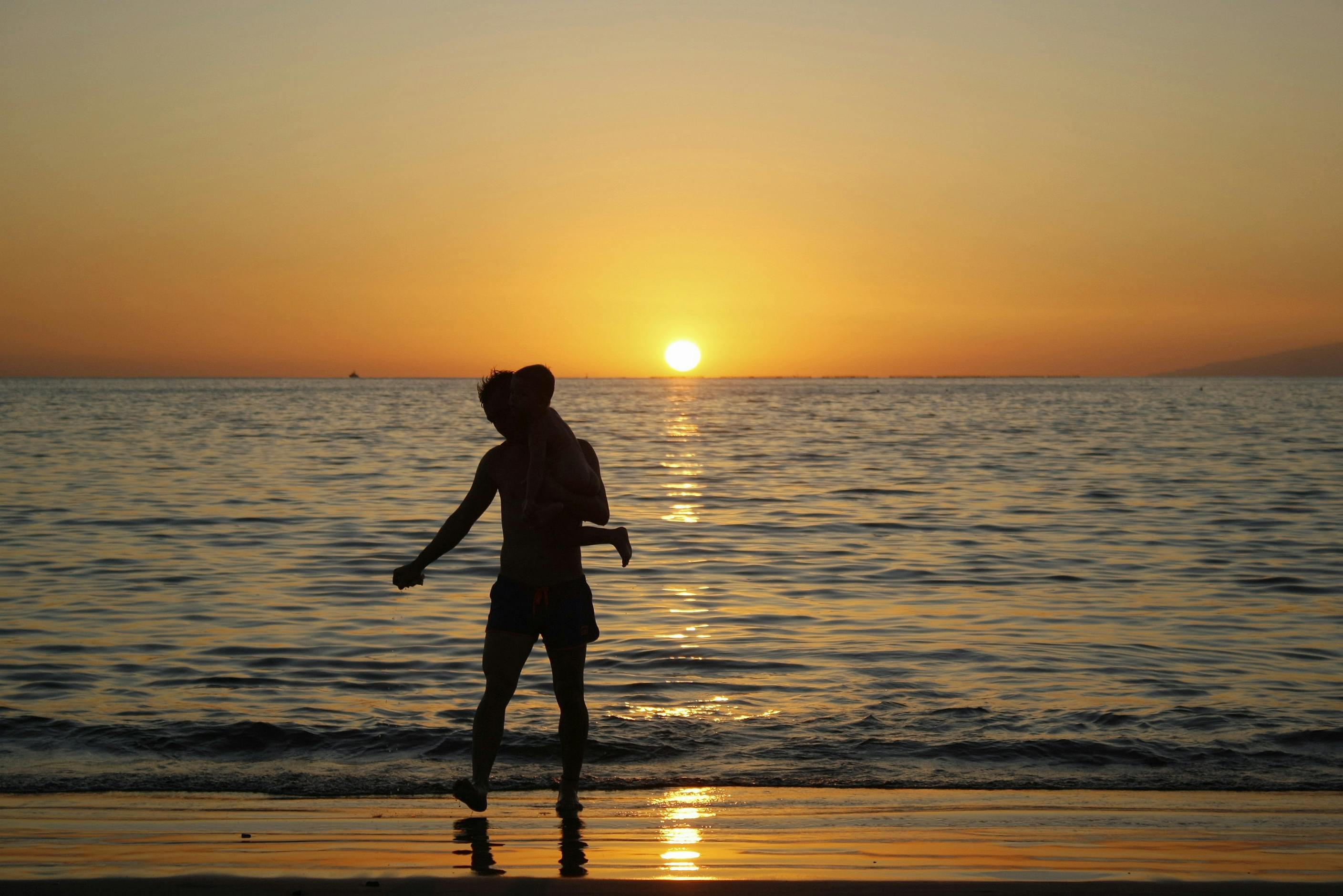 silhouette of a man carrying a child on the beach during sunset