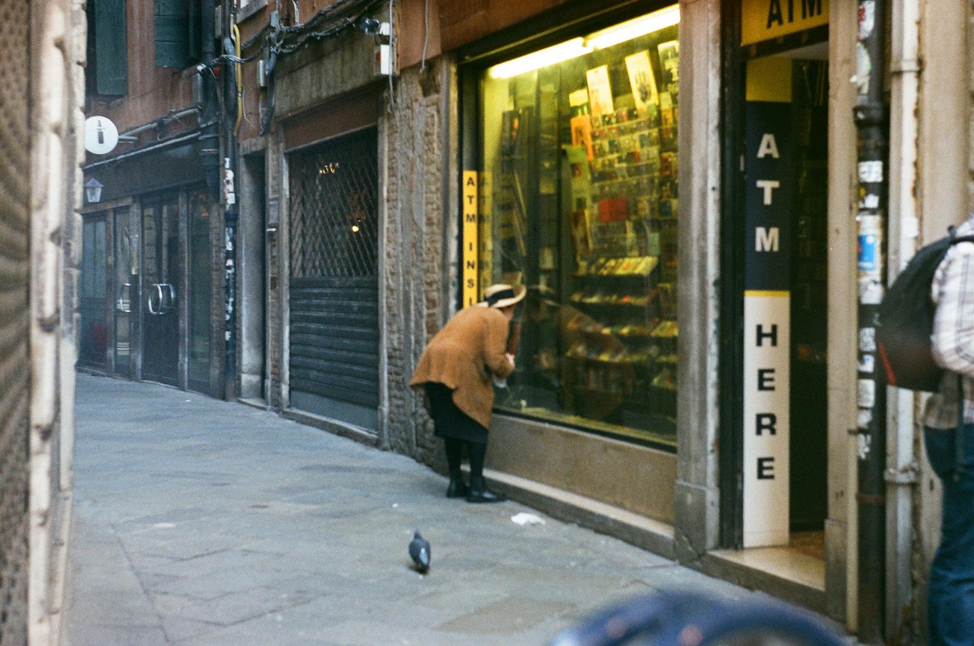 Man stands by ATM in a narrow Venice street, quietly observing the scene.