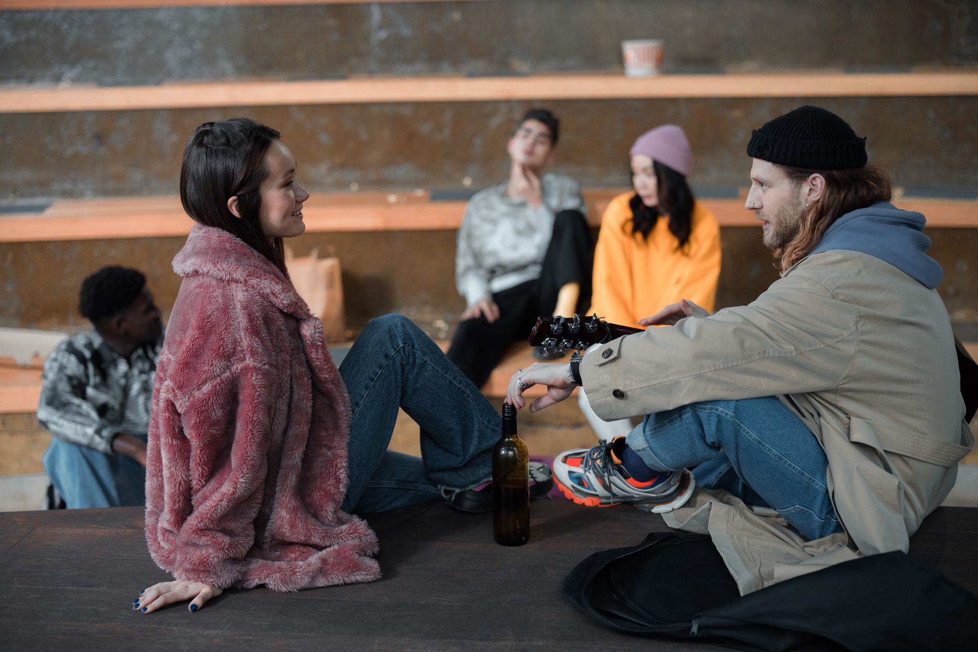 A diverse group of friends relaxing and chatting indoors at a modern amphitheater setting.