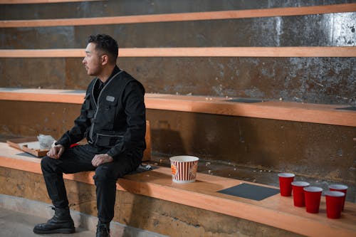 Free A Man in Black Jacket Sitting on the Bleachers Stock Photo