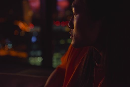 A man in profile looks out at colorful bokeh lights at night, creating a reflective mood.