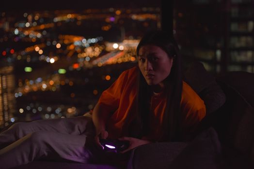 A person engrossed in gaming at night with a city skyline backdrop.