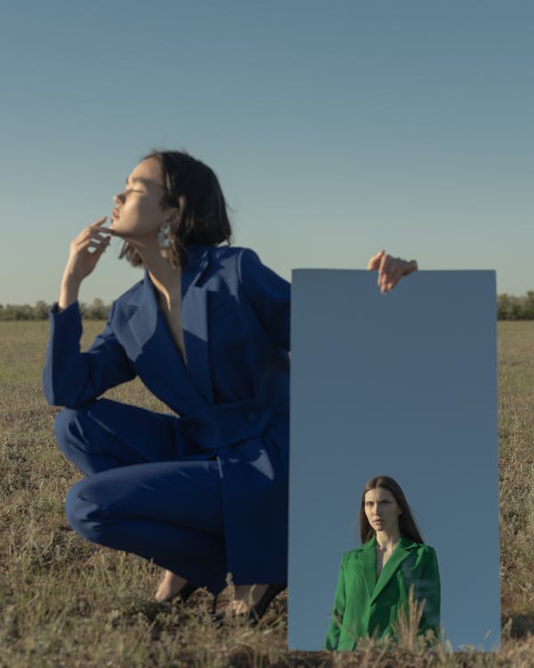 Woman Wearing Blue Suit Posing on a Field and Holding Image of a Model in Green Suit