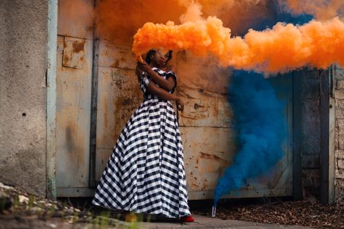 Free An artistic fashion model poses with vibrant orange and blue smoke outdoors. Stock Photo