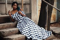 一位穿着格子连衣裙的时尚女子在树旁的台阶上摆姿势