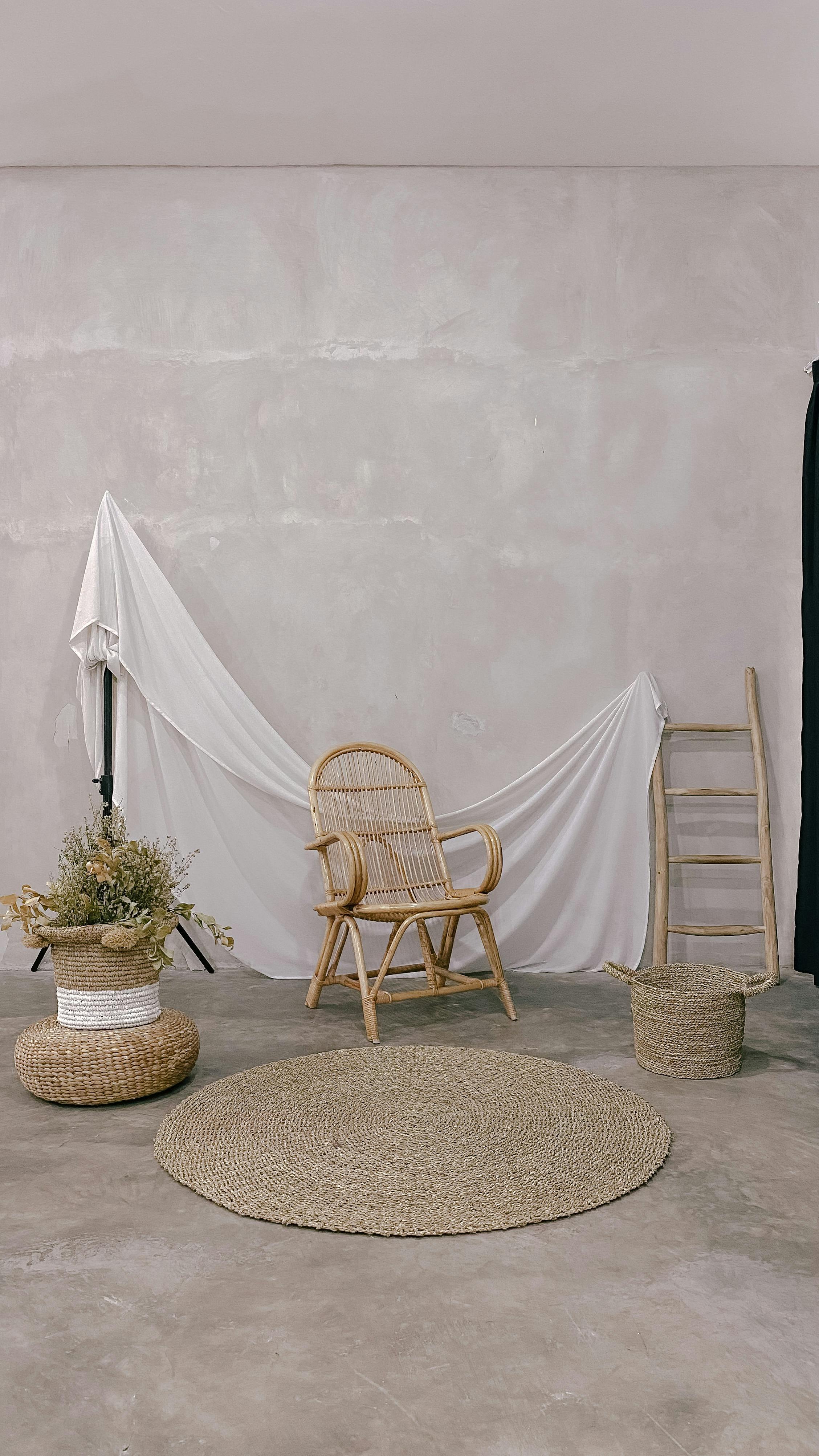 Minimalist studio setup featuring a wicker chair, woven rug, and decor against a textured wall.