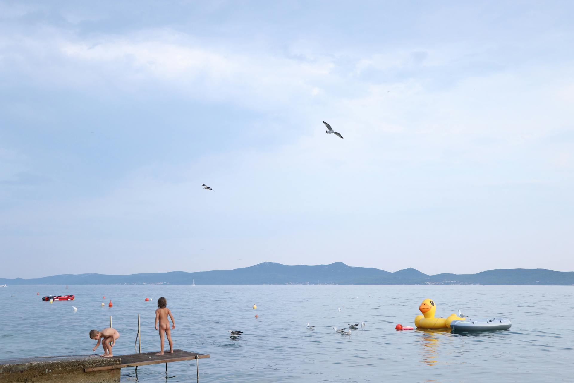 Children playing by the sea in Croatia with a large inflatable duck. Summer fun outdoors.