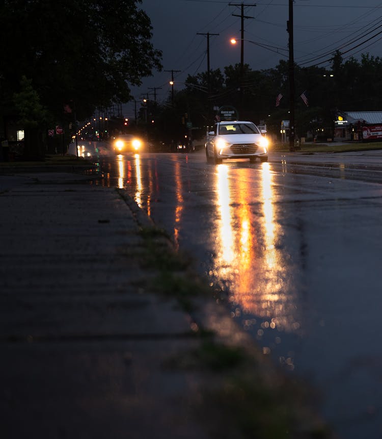 Cars With Lights On Driving Rainy Road At Night