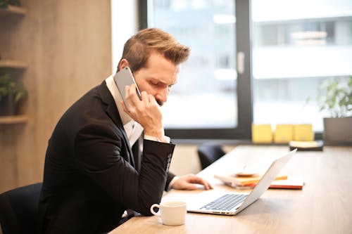 Free Man Having a Phone Call In-front of a Laptop Stock Photo