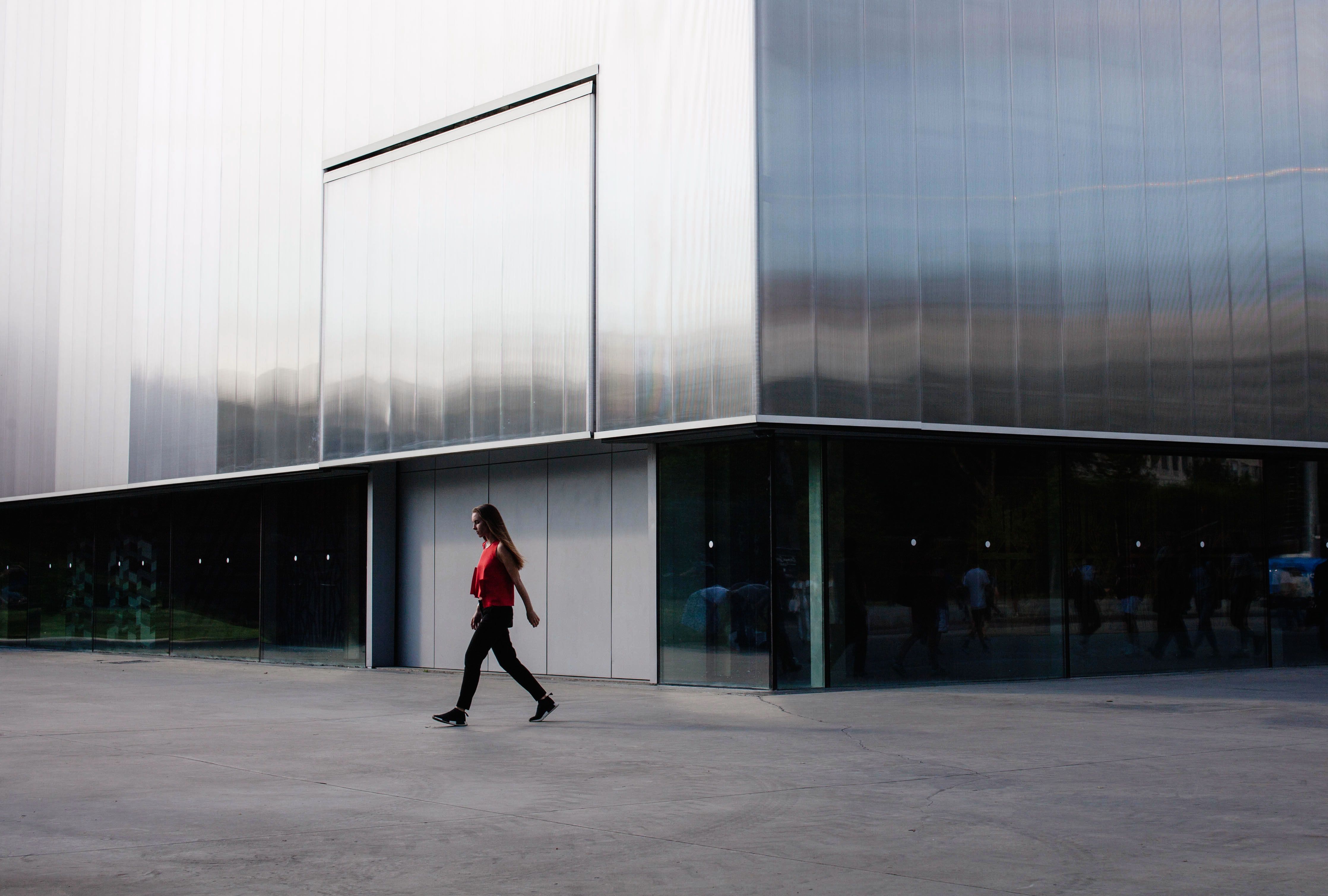 Woman walks by modern building facade in Moscow. Daylight scene with sleek architecture.