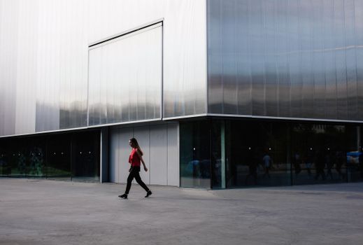 Woman walks by modern building facade in Moscow. Daylight scene with sleek architecture.