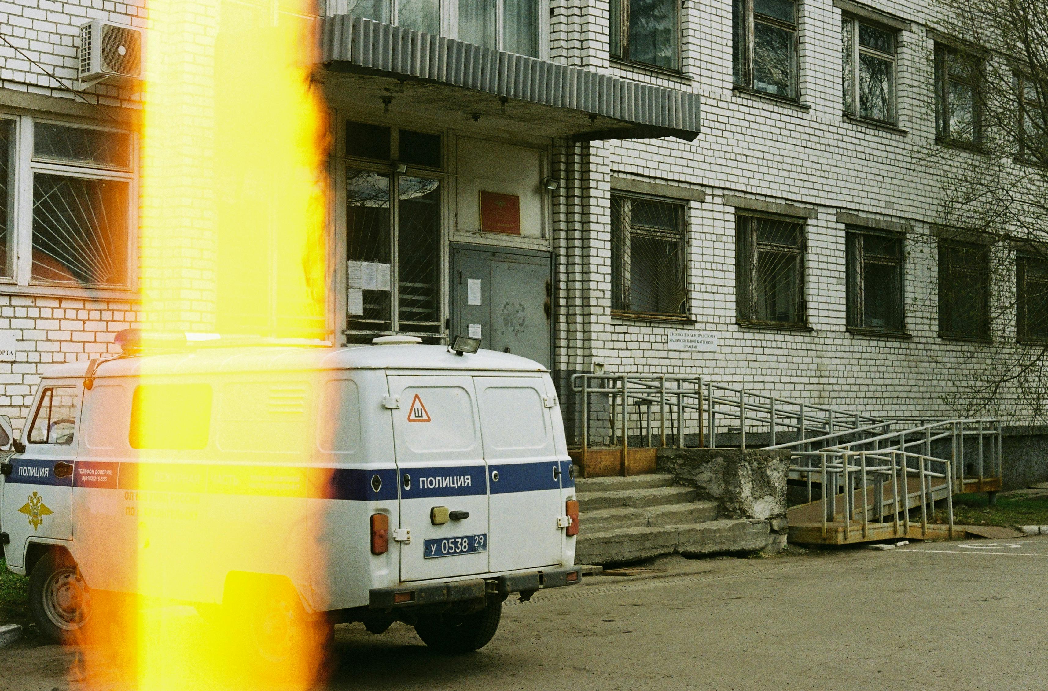 A white police van parked outside a brick building, with a distinctive light leak effect.