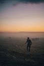 Man in Black Jacket Walking on Green Grass Field during Sunset