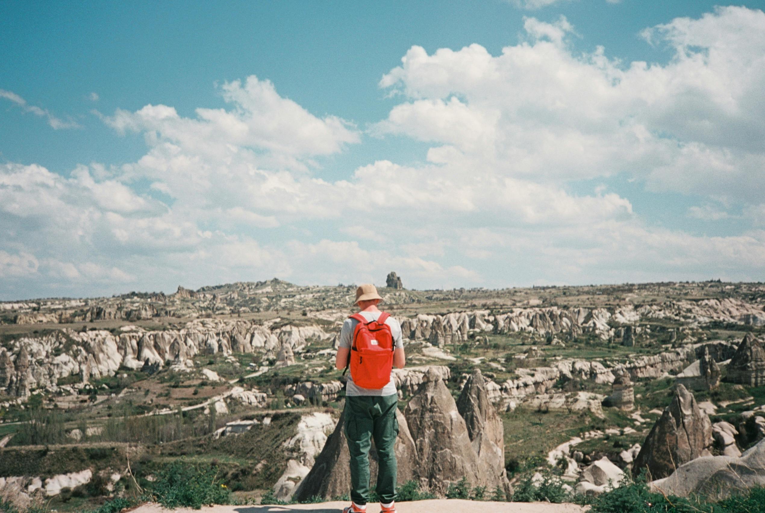 Man with a Red Backpack Standing While near the Rocky View · Free Stock