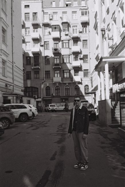 Black and white photo of a man standing in an urban alley with surrounding buildings.
