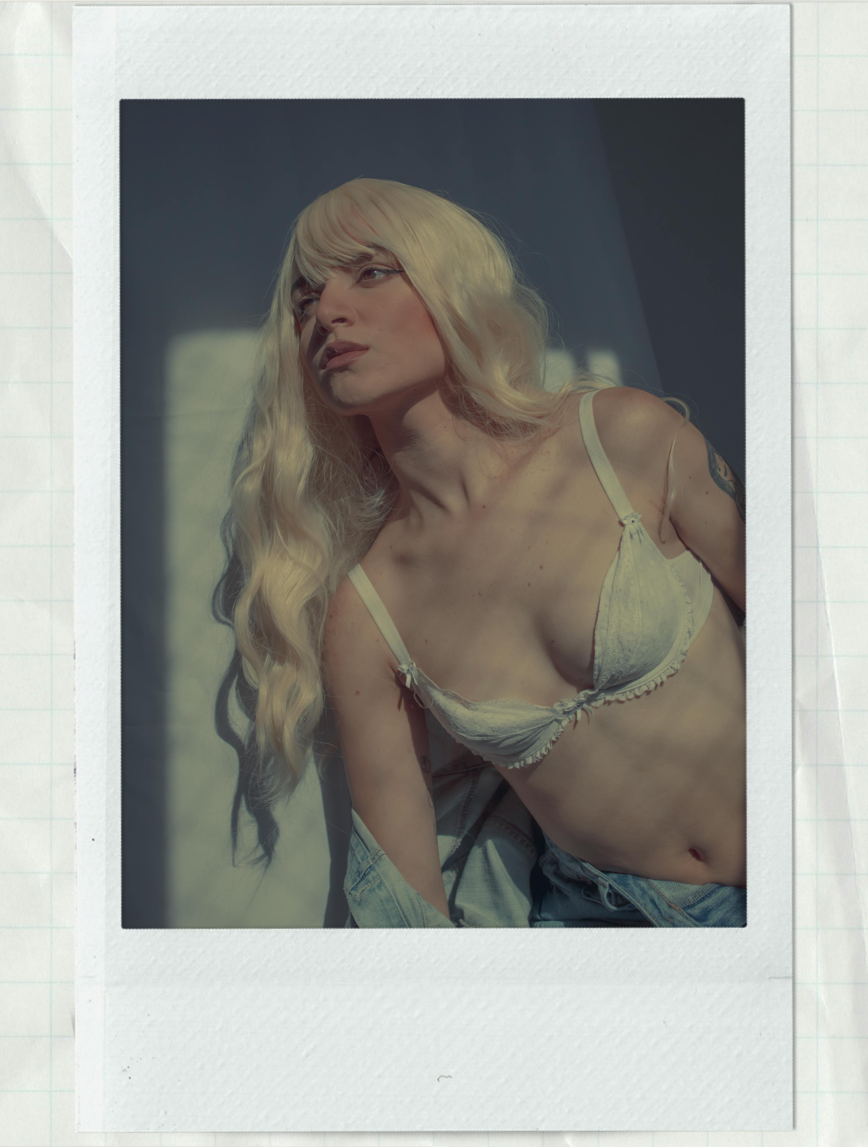 Caucasian woman with blonde hair posing in white lingerie in a Polaroid photograph.