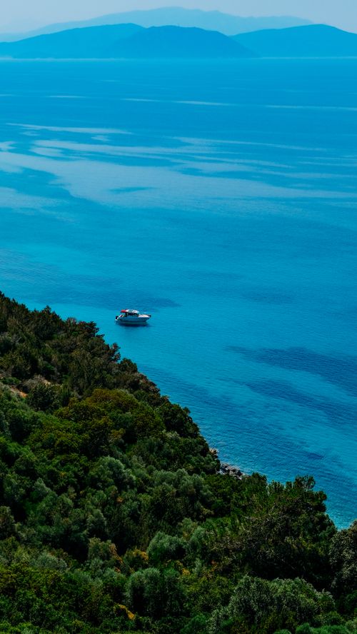 Free A tranquil aerial view of a boat floating on a serene ocean bay surrounded by lush greenery. Stock Photo