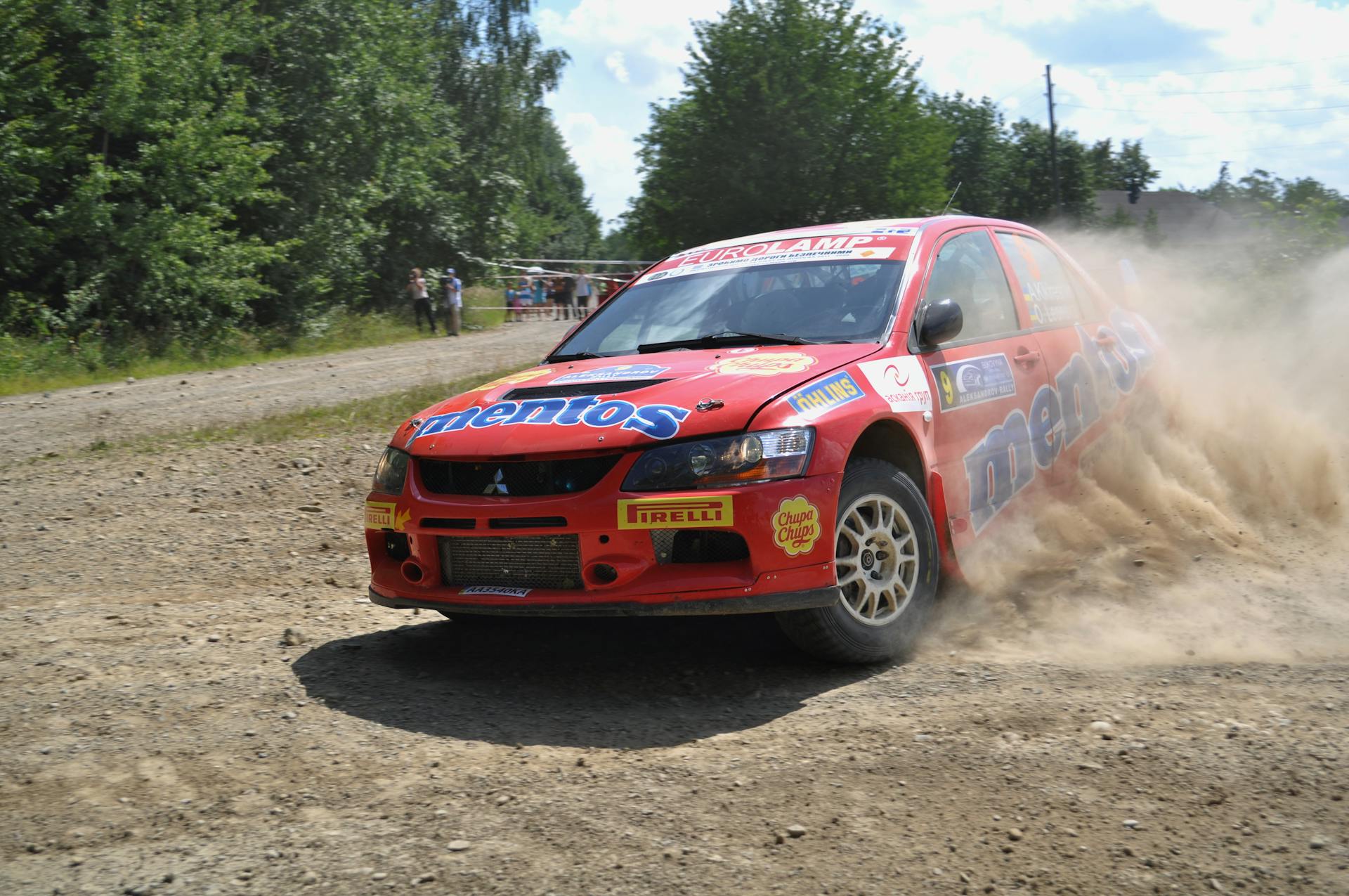 Red Mitsubishi Lancer Evo speeding through a dirt track during a thrilling rally race with dust clouding behind.