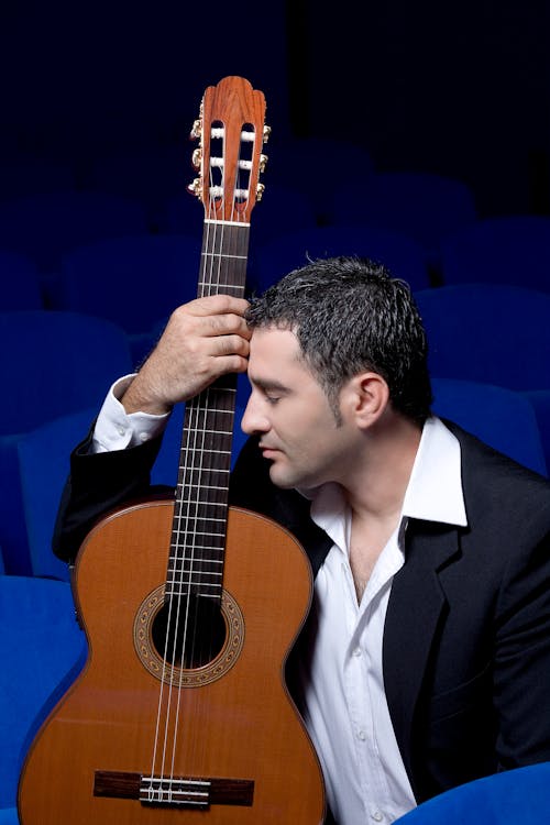 Man in a Black Suit Holding a Brown Acoustic Guitar